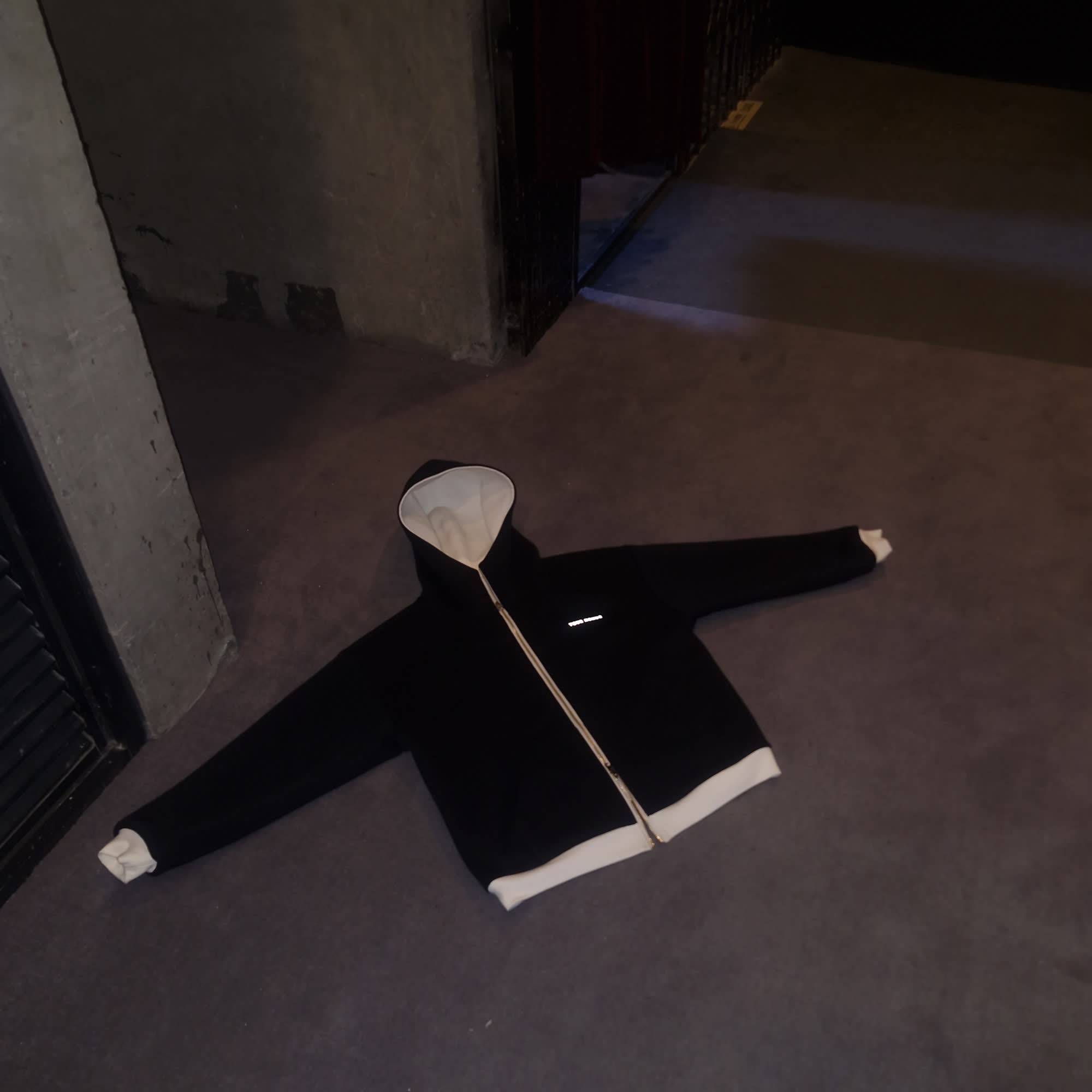 Reversible hoodie laid flat showing the black exterior with cream interior at the hood